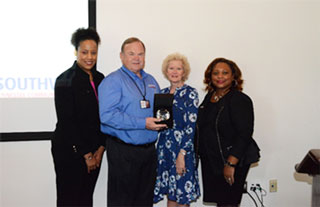 Ambassador of the Year Ron Wells accepts his award alongside Daphne Thomas, his wife Teresa Wells and President Tracy D. Hall