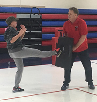 English Instructor Tiffany Parish Akin follows through with Officer Merritt’s instructions on how to perform the “kick to the groin” self-defense technique at the R.A.D. Systems training for female employees.