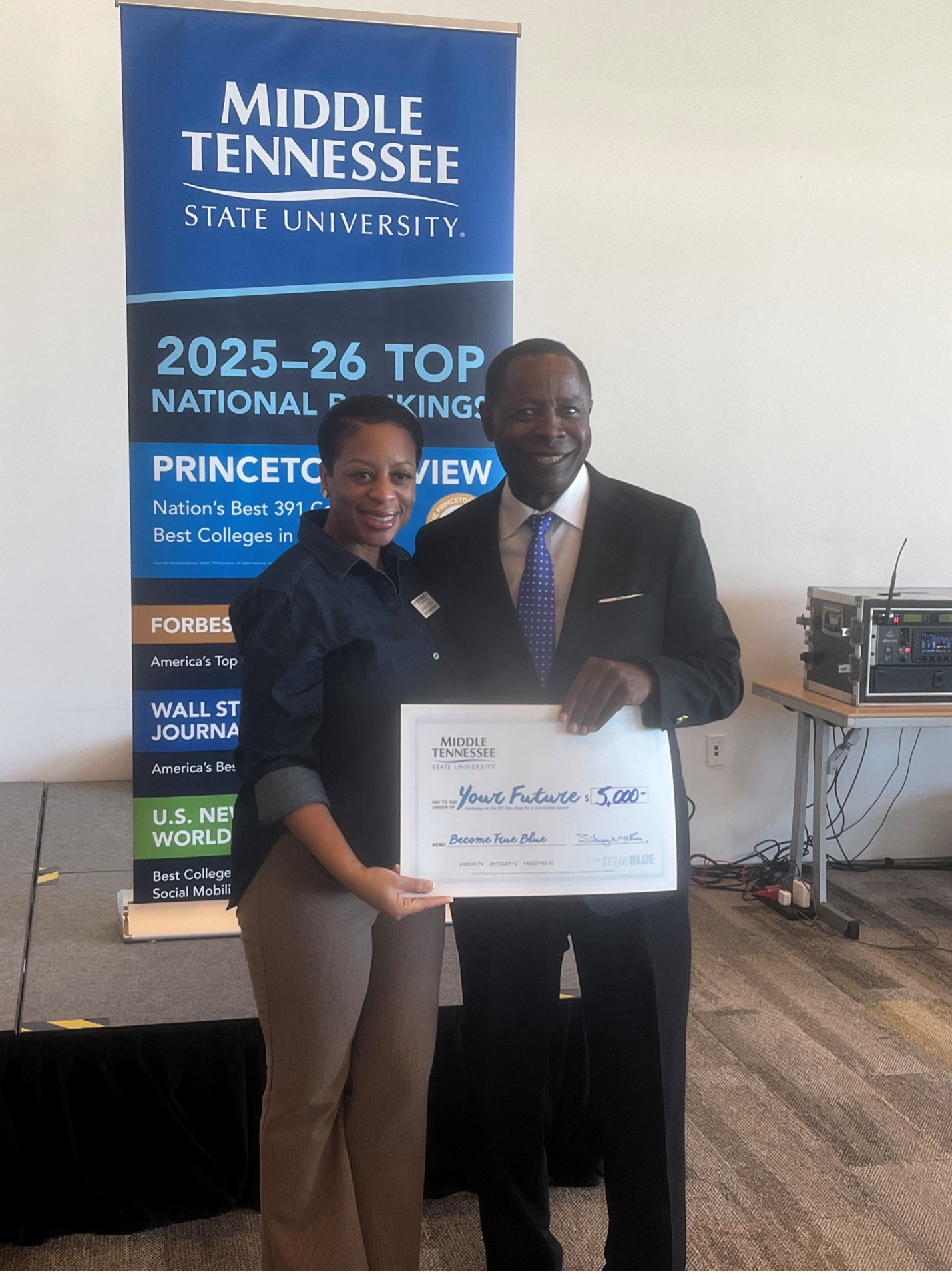 Man handing pretend check to woman that says MTSA pay to the order Your Future for 5000