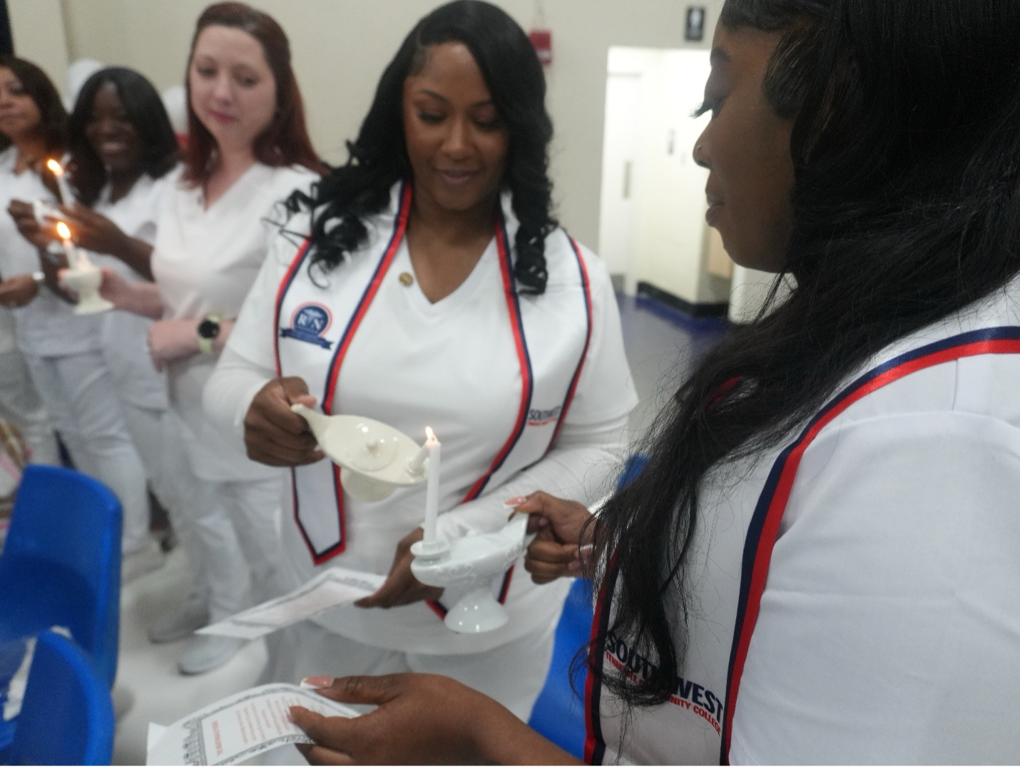 Nursing students in white uniforms participate in a candlelight ceremony. Each person lights a candle from another, symbolizing tradition and unity. “RN” and “Southwest Tennessee Community College” are visible on uniforms. Esma and Dr. Hall standing in front of Tennessee and United States flags