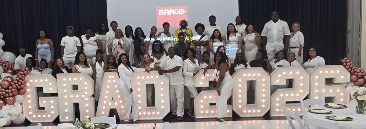 Students dressed in white behind illuminated letters spelling Grad 2026